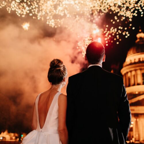 Lovely married couple stand backs to camera, admire beautiful firework in night sky